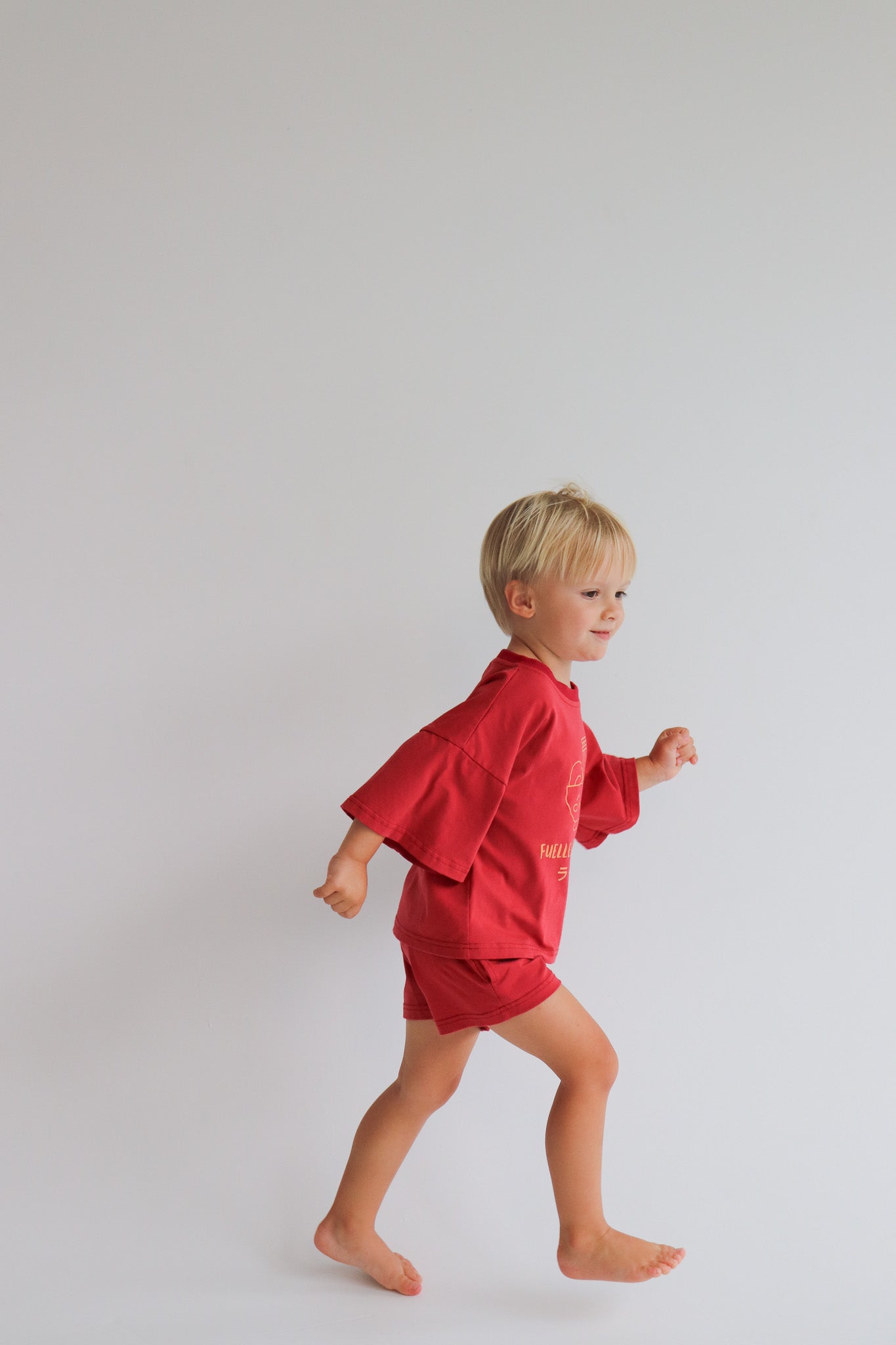 Child wearing an oversized red t shirt and short set with an orange ramen bowl logo with 'Fuelled by ramen' writing