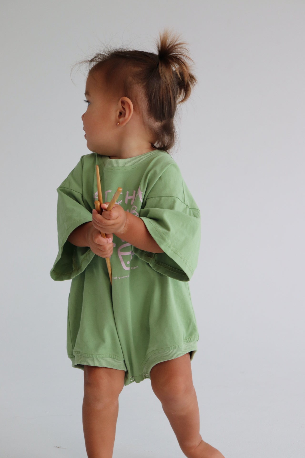 Child wearing an oversized green romper with a pink matcha club logo.
