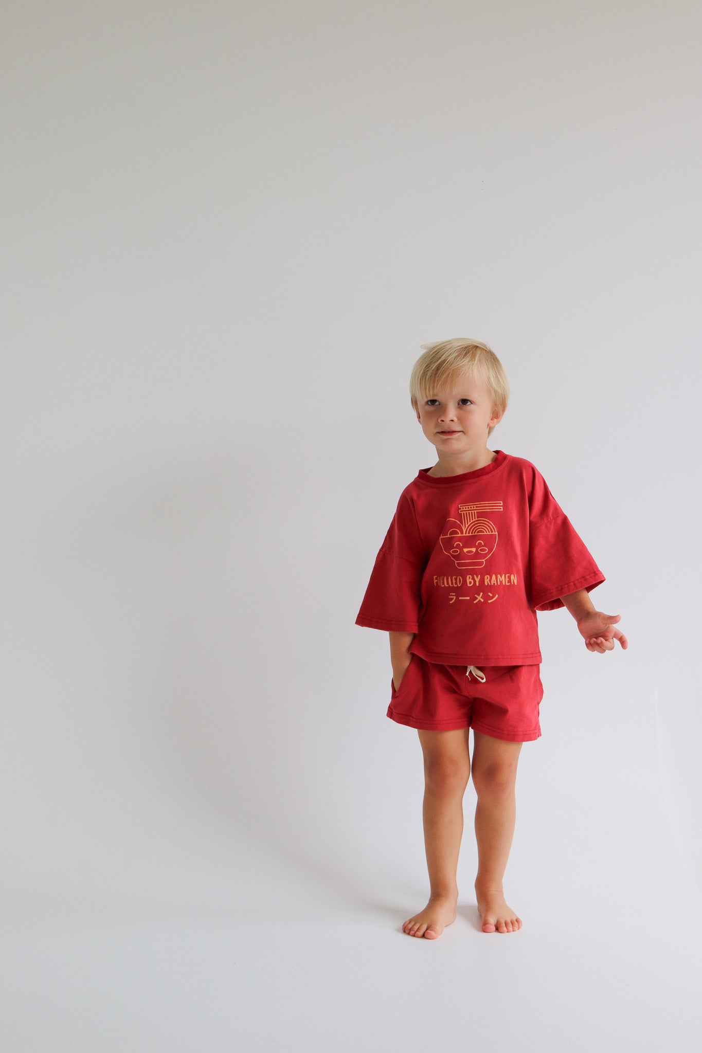 Child wearing an oversized red t shirt and short set with an orange ramen bowl logo with 'Fuelled by ramen' writing