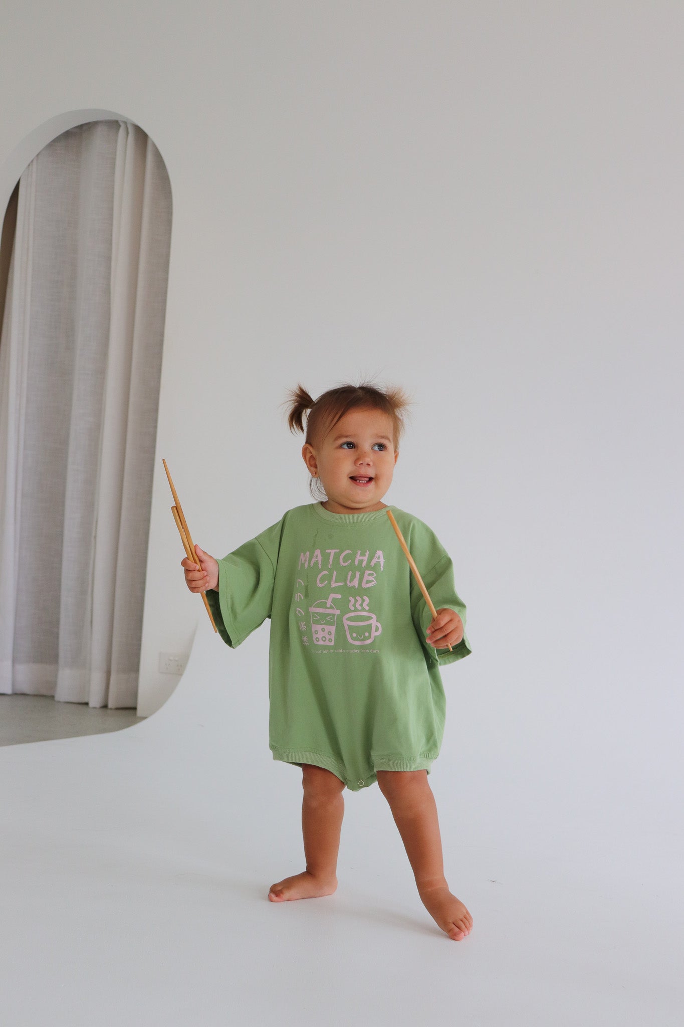 Child wearing an oversized green romper with a pink matcha club logo.