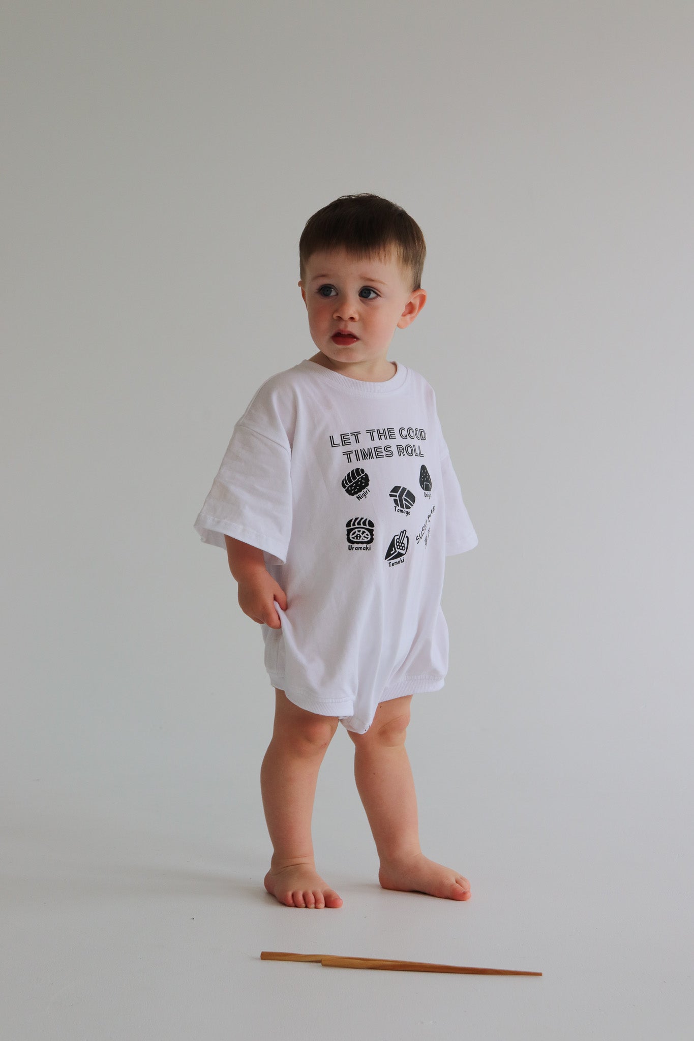Child wearing a white oversized romper with a black sushi logo 'Let the good times roll'