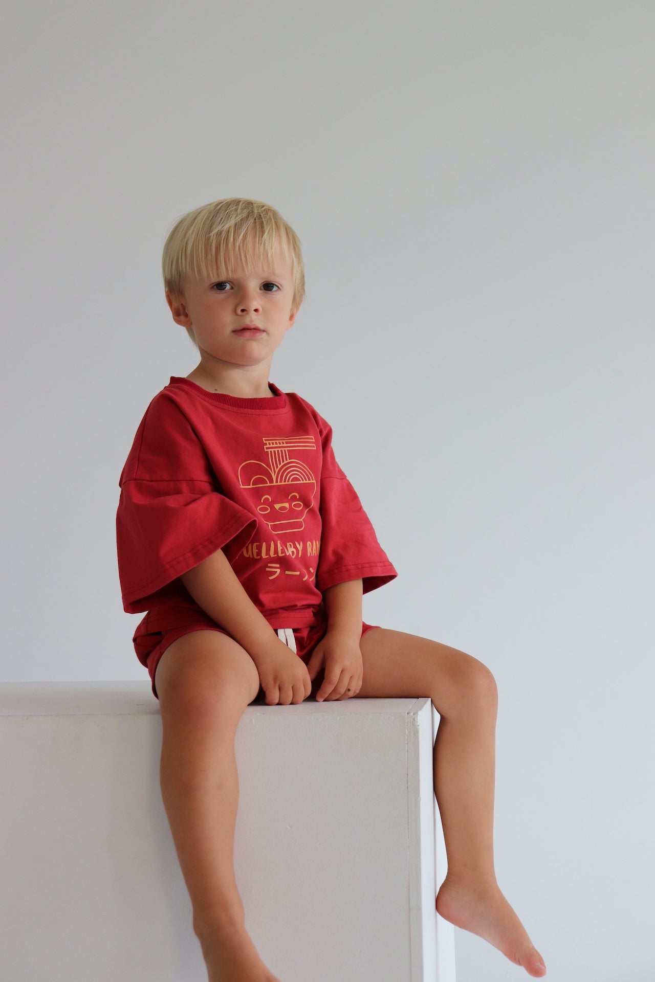 Child wearing an oversized red t shirt and short set with an orange ramen bowl logo with 'Fuelled by ramen' writing