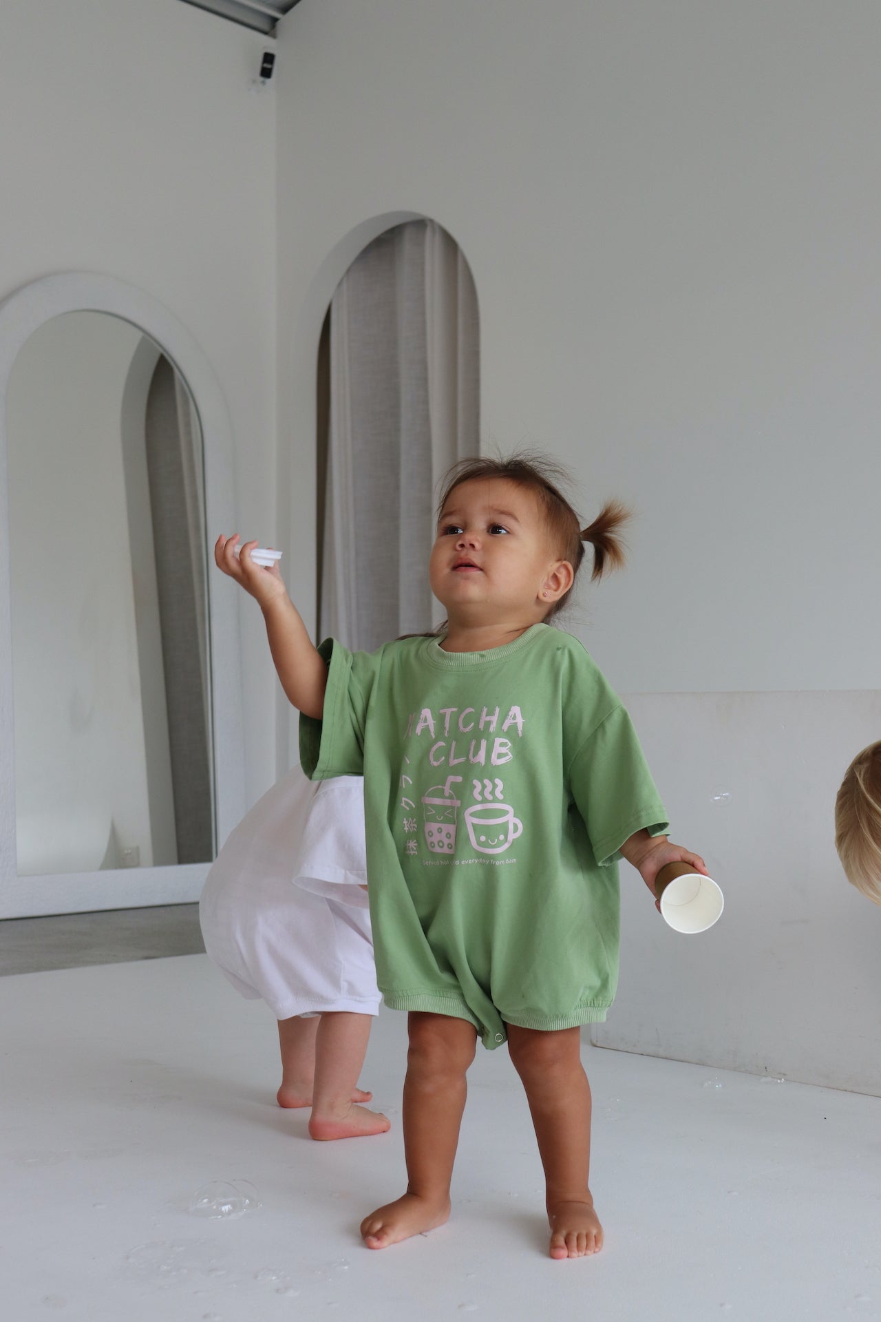 Child wearing an oversized green romper with a pink matcha club logo.
