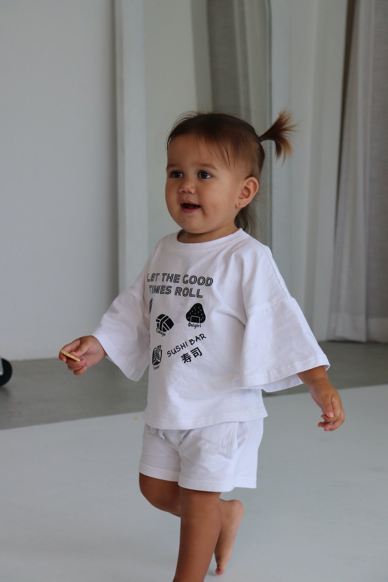 Child wearing a white oversized t-shirt and shorts with a black sushi logo 'Let the good times roll'