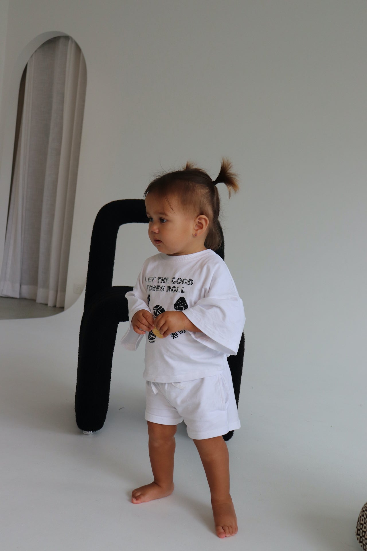Child wearing a white oversized t-shirt and shorts with a black sushi logo 'Let the good times roll'