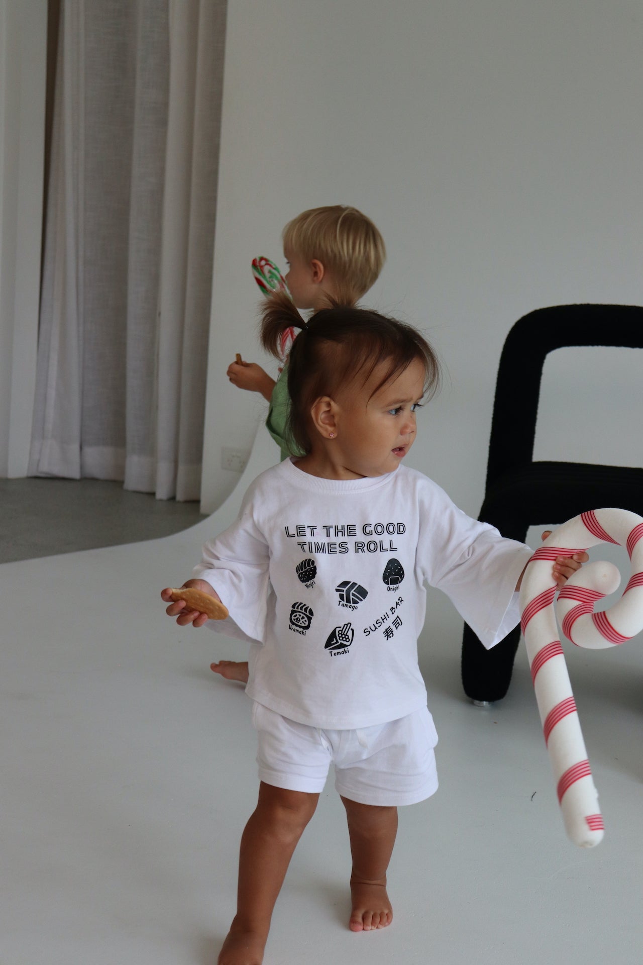 Child wearing a white oversized t-shirt and shorts with a black sushi logo 'Let the good times roll'