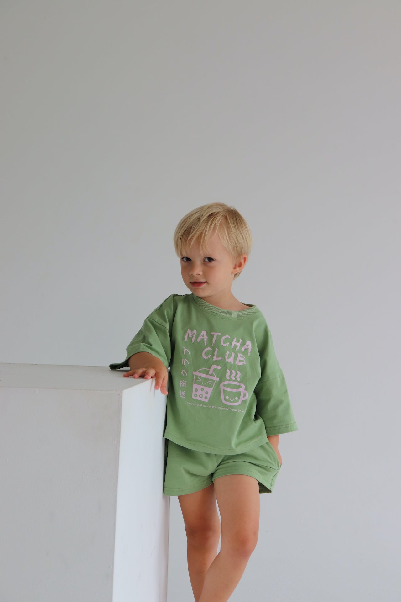 Child wearing an oversized green t-shirt set with a pink matcha club logo.