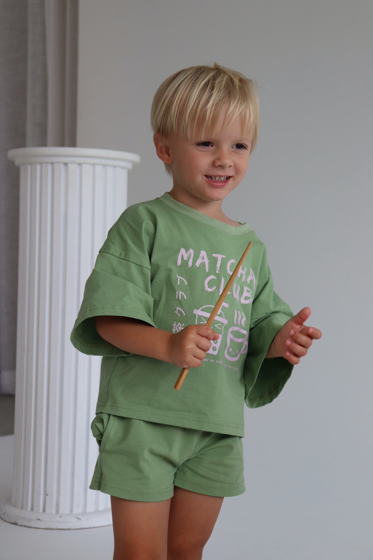 Child wearing an oversized green t-shirt set with a pink matcha club logo.