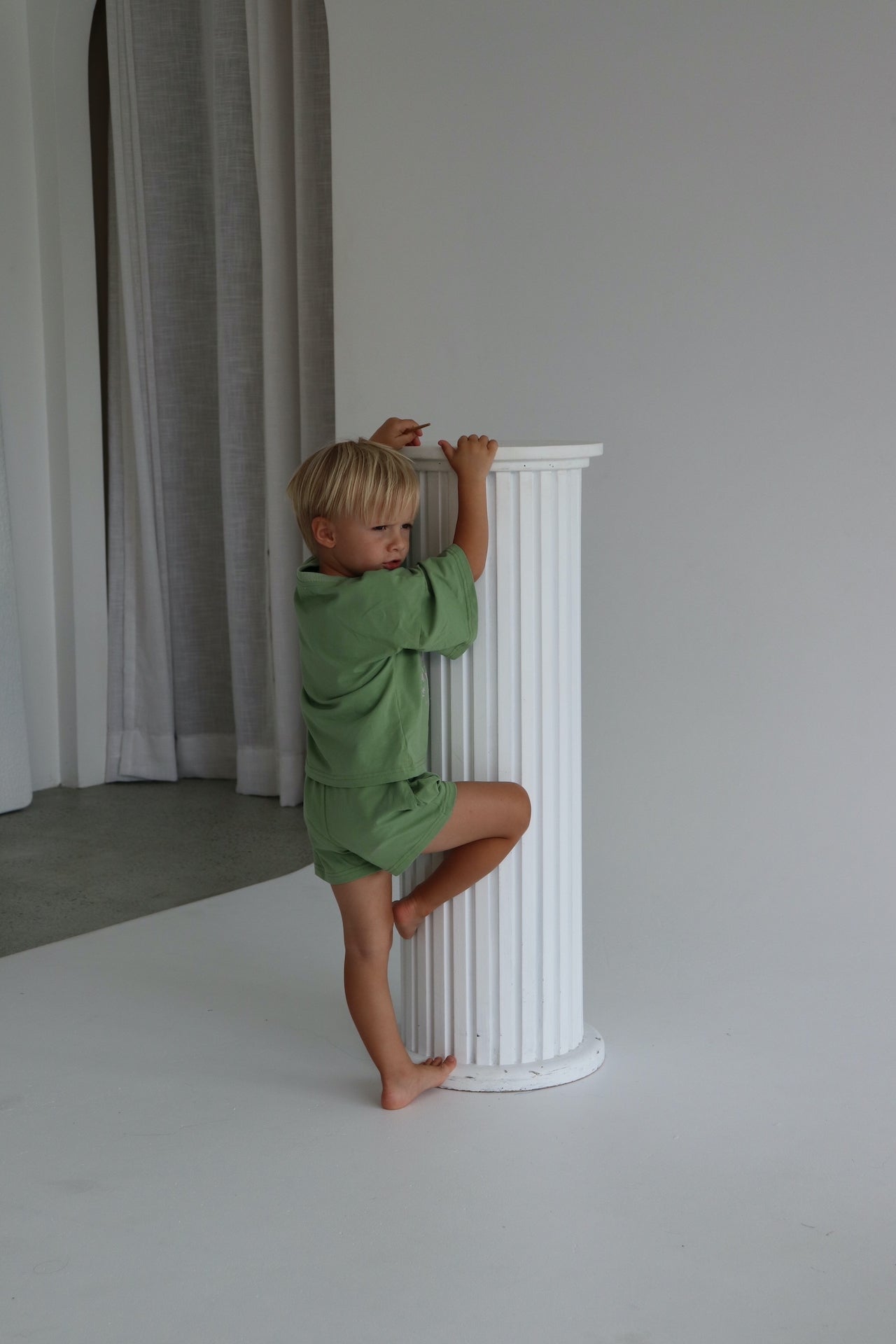 Child wearing an oversized green t-shirt set with a pink matcha club logo.