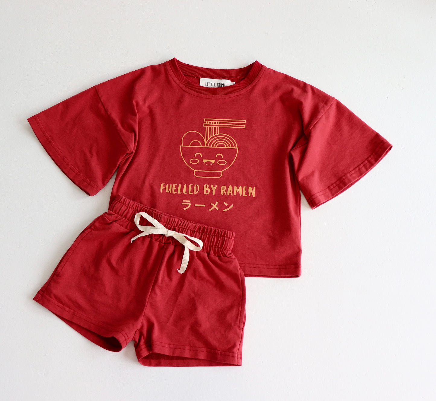Flat lay photo of on oversized red t shirt and short set with an orange ramen bowl logo with 'Fuelled by ramen' writing