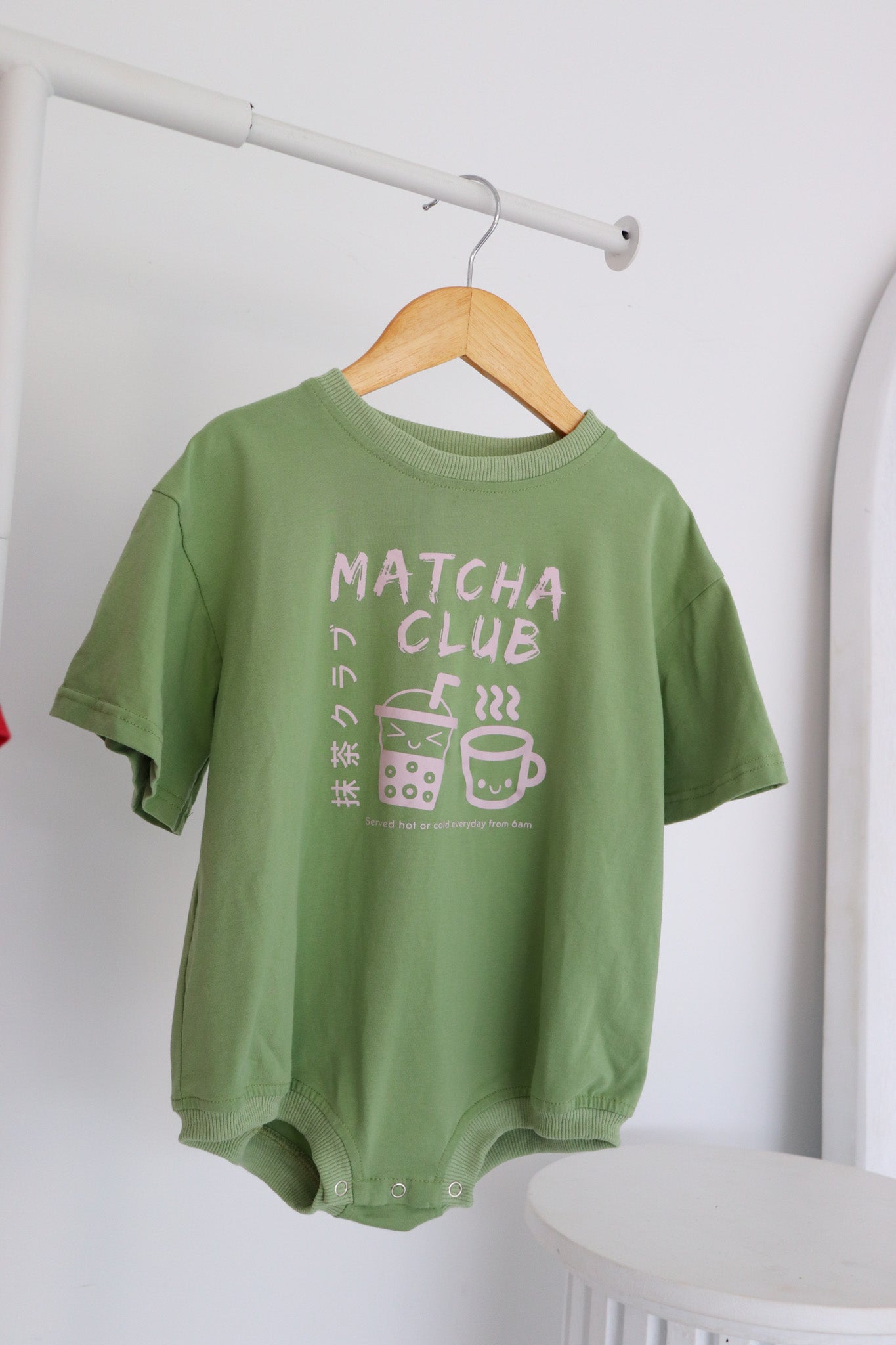 A hanging oversized green romper with a pink matcha club logo.